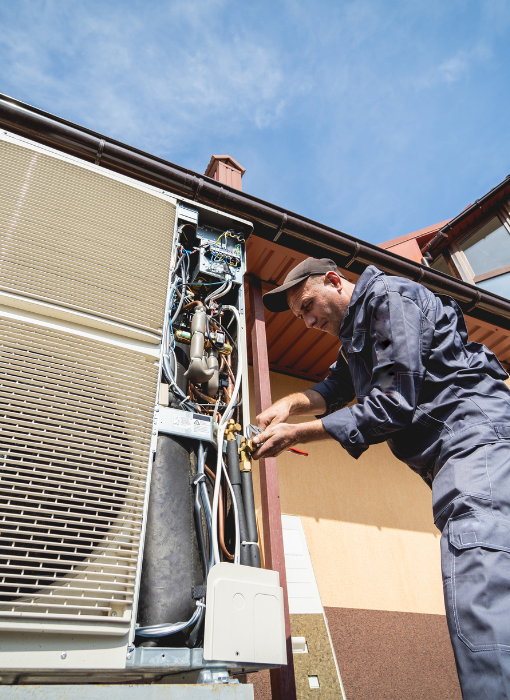 A man in a blue shirt repairs an air conditioner, demonstrating technical skills and focus on the task at hand.