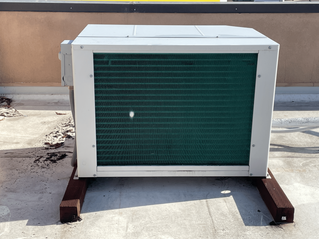 . A green air conditioner positioned on a rooftop, blending with the surroundings under a clear blue sky.